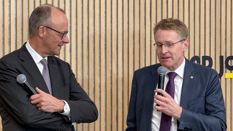 Bundeskanzler Friedricht Merz (l.) und Ministerpräsident Daniel Günther (r.) stehen auf einem Podium mit Mirkrophonen in den Händen.