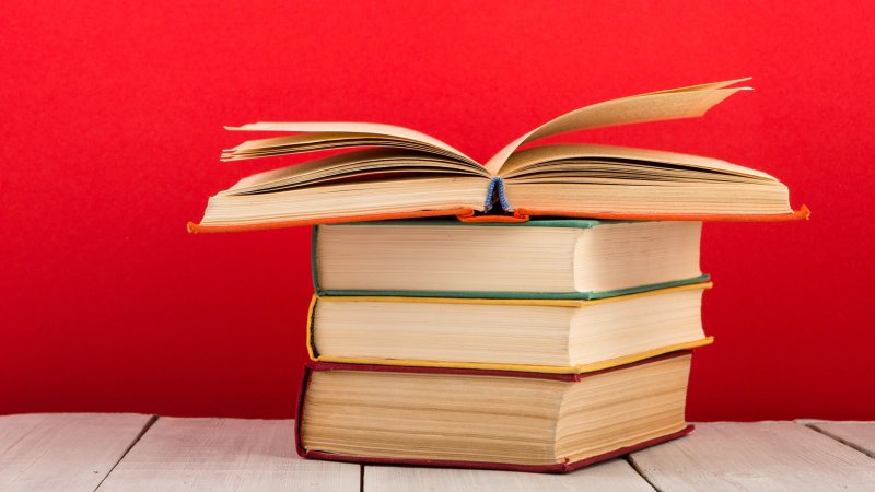 Ein aufgeschlagenes Buch liegt auf einem Bücherstapel.