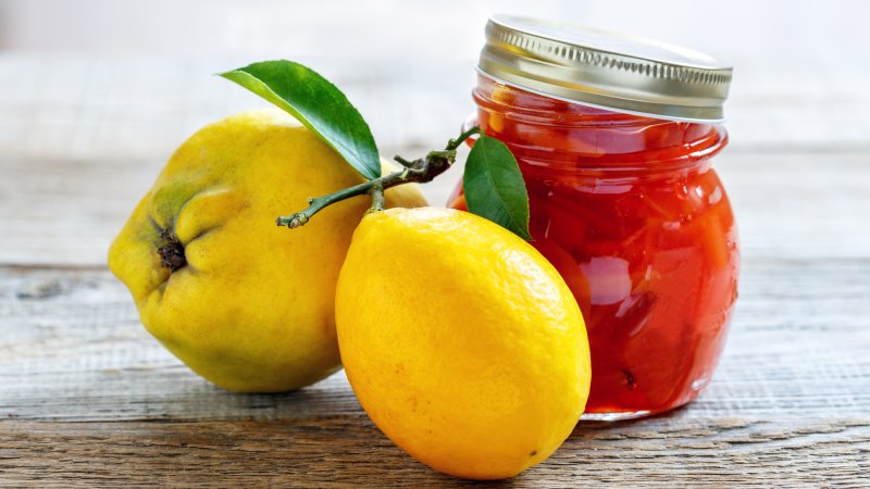 Reife Quitten sowie ein Glas mit Quittengelee und -marmelade.