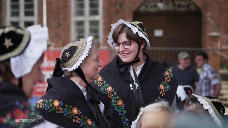 Zwei Frauen in traditionellen Trachten lächeln sich zu.