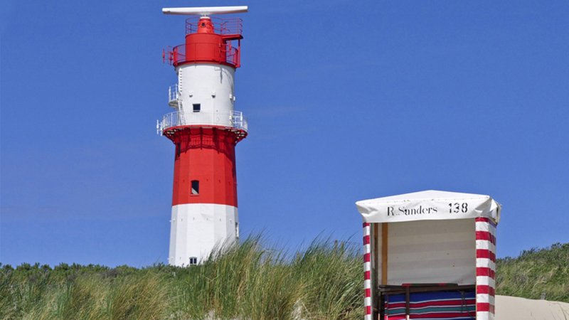 Ein rot-weißer Leuchtturm und ein Strandkorb in den Dünen.