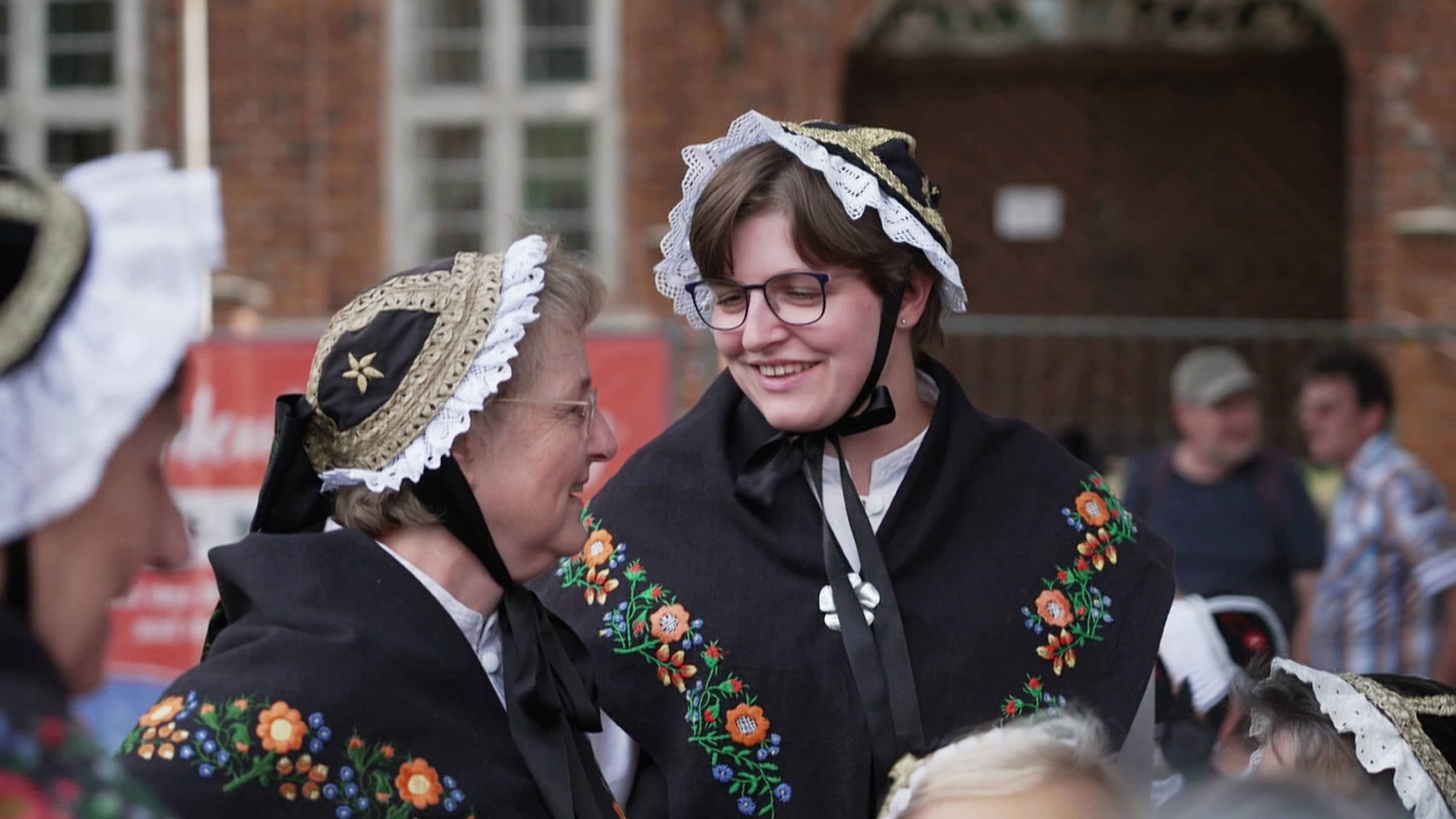 Zwei Frauen in traditionellen Trachten lächeln sich zu.