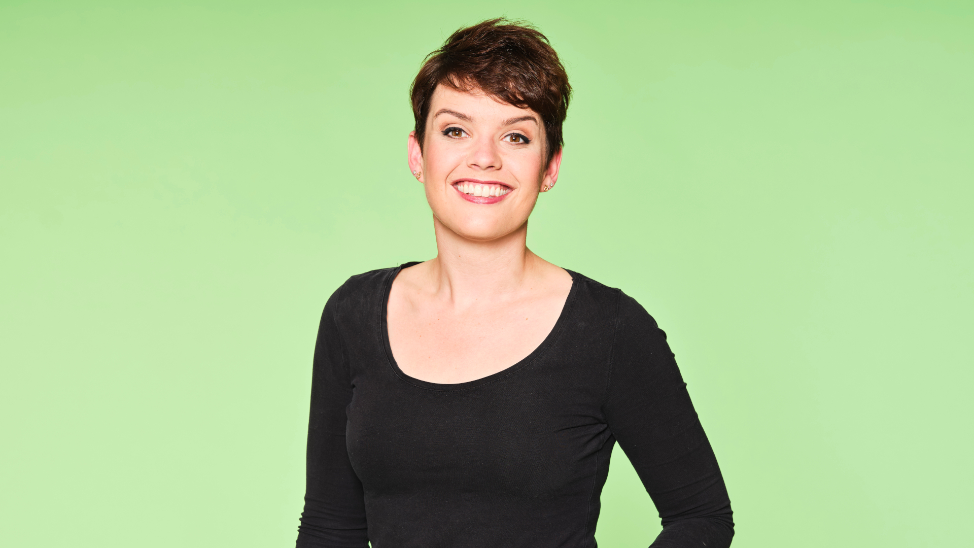Ein Frau steht vor einem grünen Hintergrund und lächelt in die Kamera.