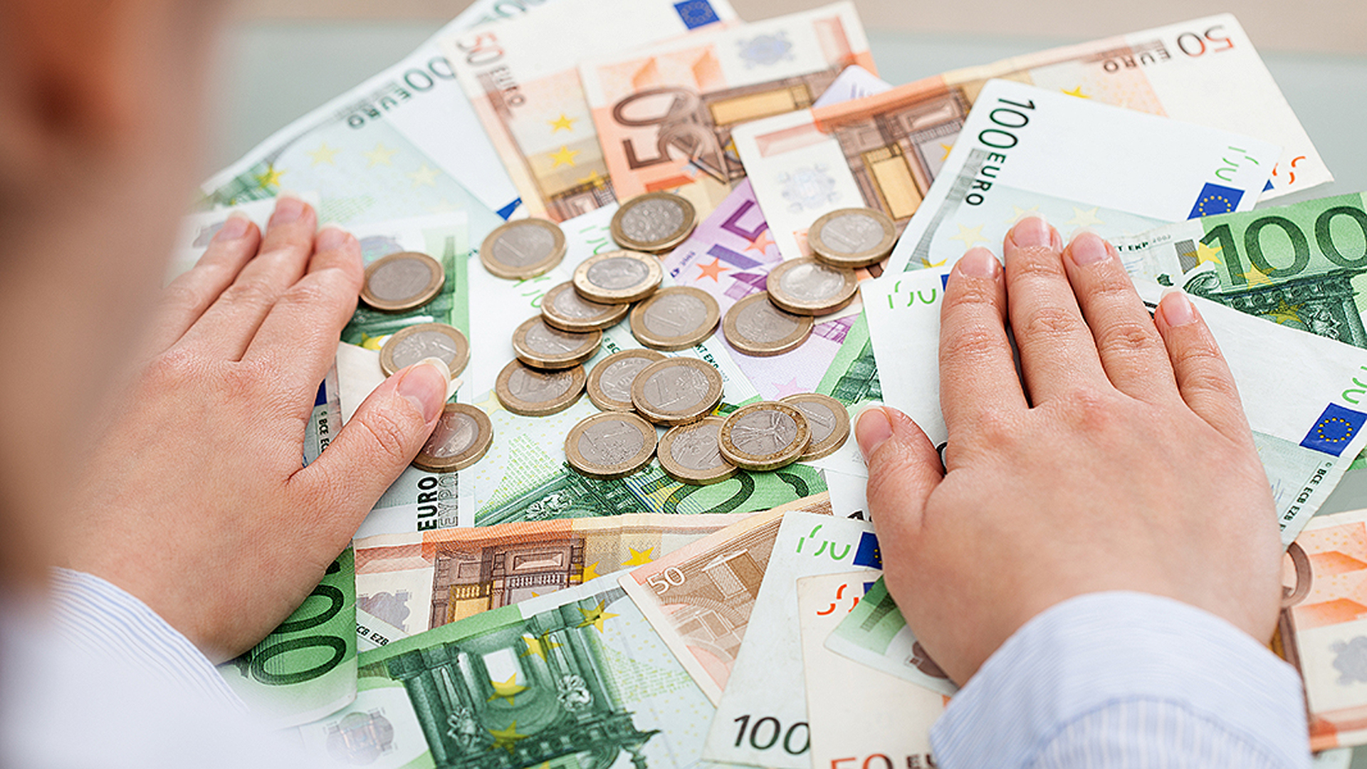 Person legt ihre Hände auf angehäuftes Geld.