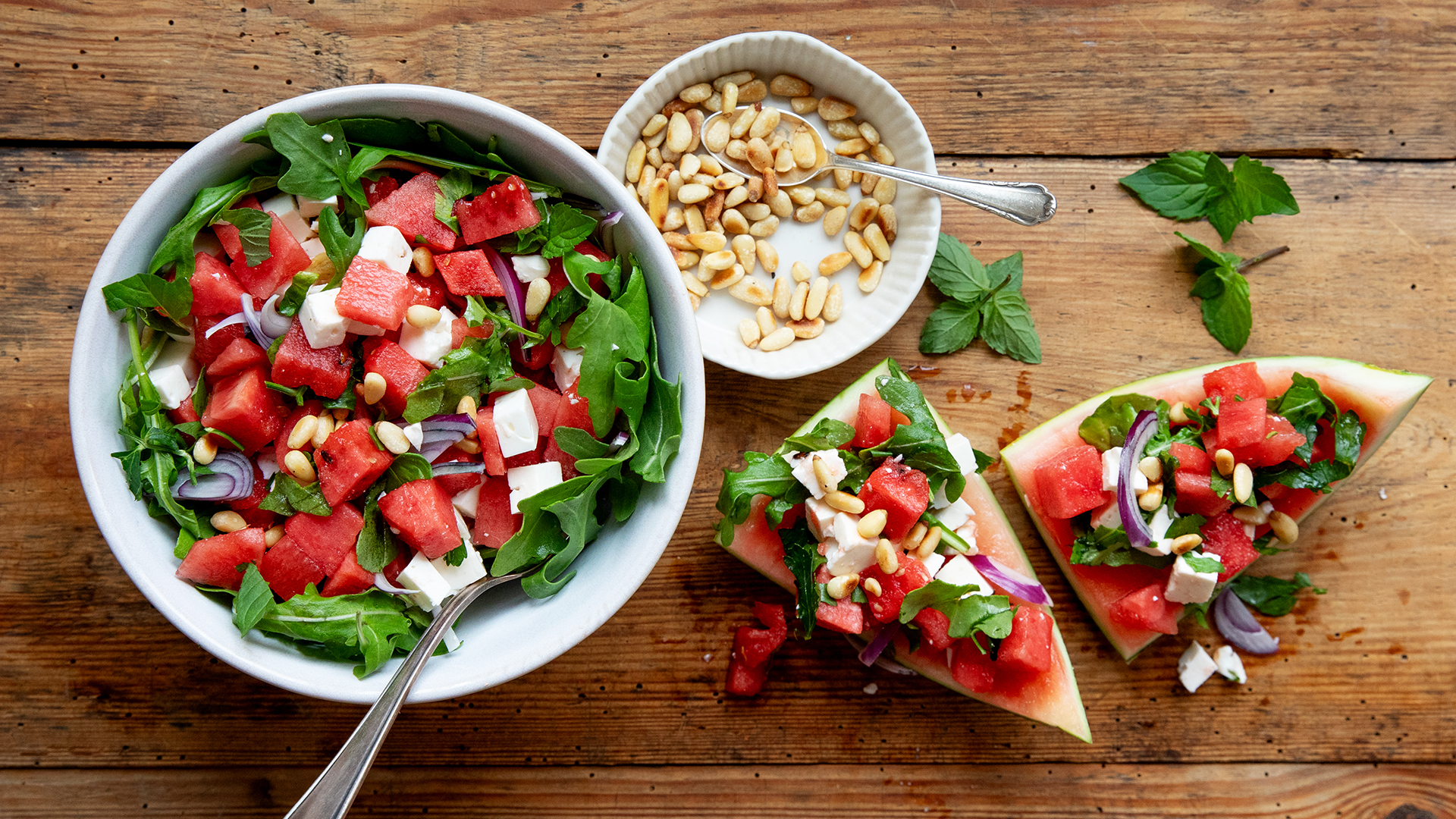 Eine Schale mit einem Melonen-Rucola-Salat, daneben ein Schälchen mit Pinienkernen.