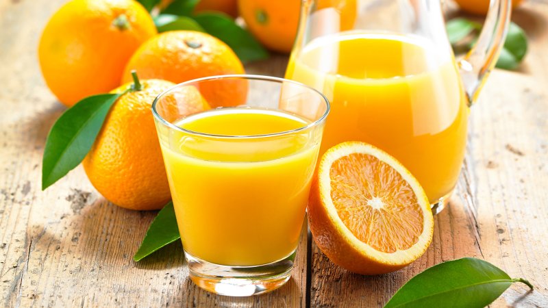 Orangensaft in einem Glas und einer Karaffe, daneben liegen frische Orangen.