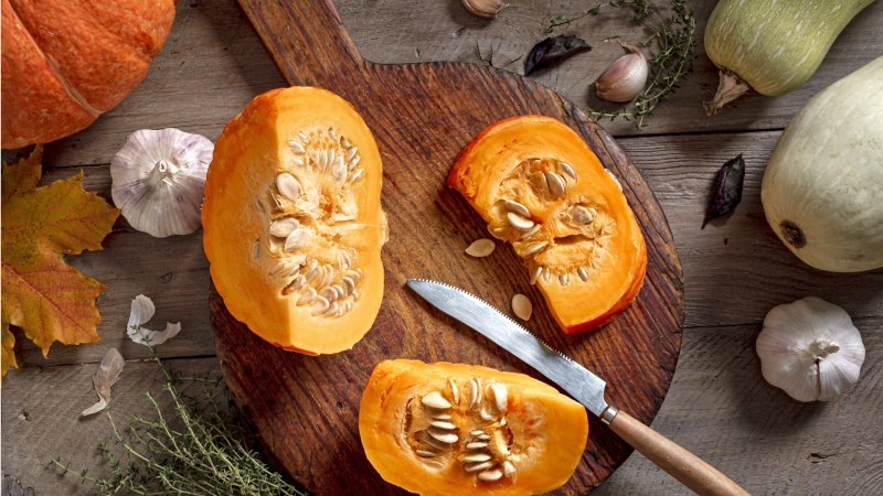 Ein in Stücke geteilter orangefarbener Kürbis mit Messer auf einem Holzbrett