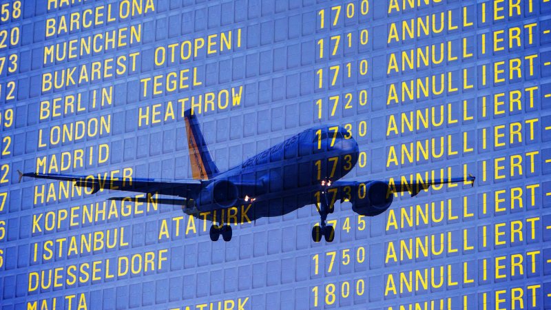 Eine Tafel am Flughafen zeigt mehrere ausgefallene Flüge. Durch die Anzeige schimmert ein Flugzeug hindurch.