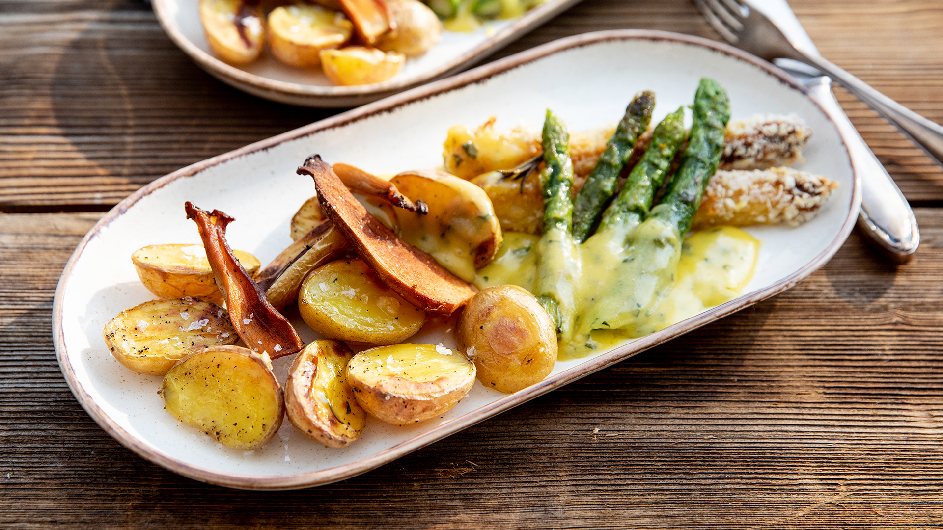 Weißer und Grüner Spargel mit Basilikum-Hollandaise, Ofenkartoffeln und Pilz-Chips auf einem Teller serviert.
