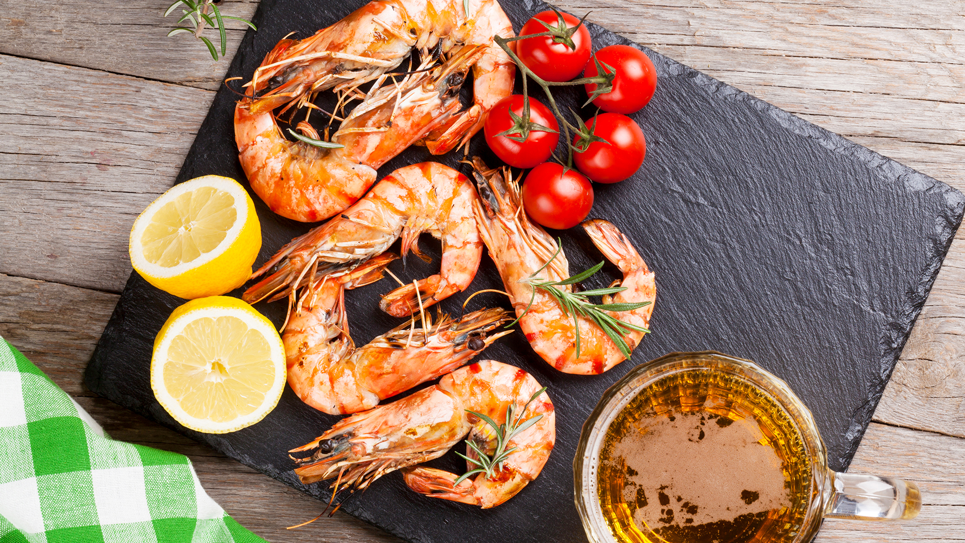 Auf einer Schiefertafel liegen gegarte Garnelen, einige Tomaten sowie Zitronenscheiben.