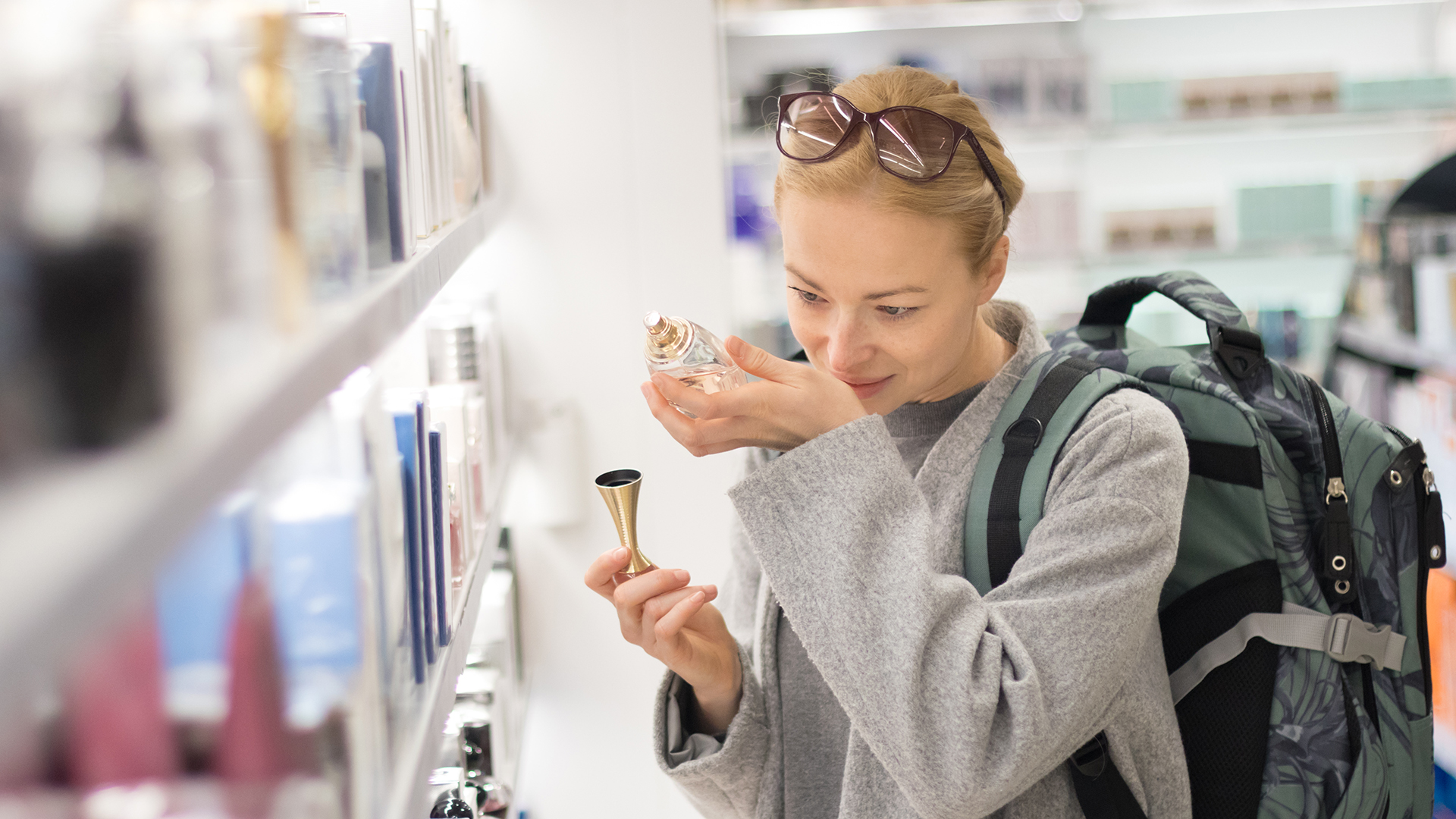 Eine Frau mit Rucksack probiert am Flughafen Parfum im Duty Free Shop.