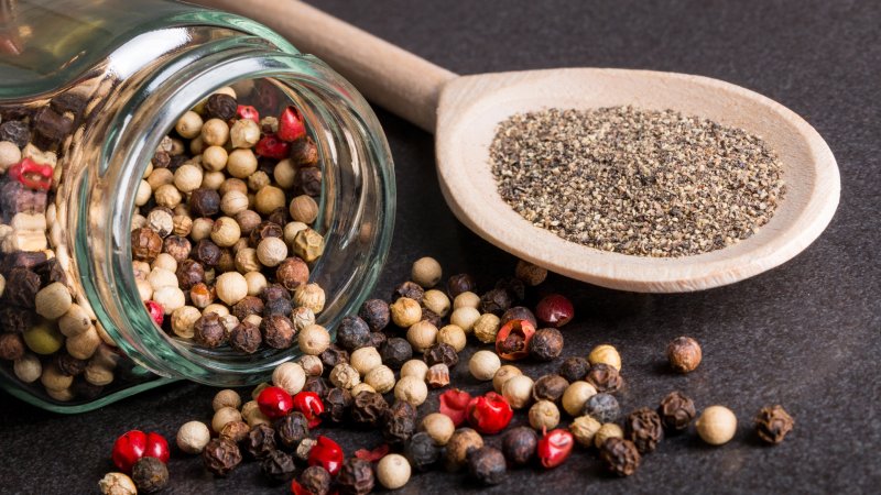 Verschieden farbige Pfefferkörner im Glas und auf einem Holzlöffel