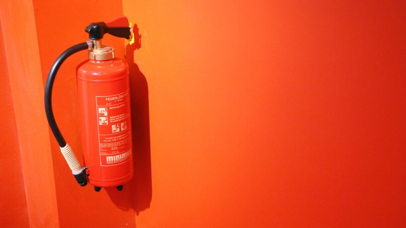 Ein Feuerlöscher hängt an einer orangefarbenen Wand.