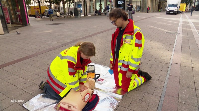 Zwei Mitarbeitende des ASB zeigen in der Fußgängerzone an einer Puppe eine Herzdruckmassage.